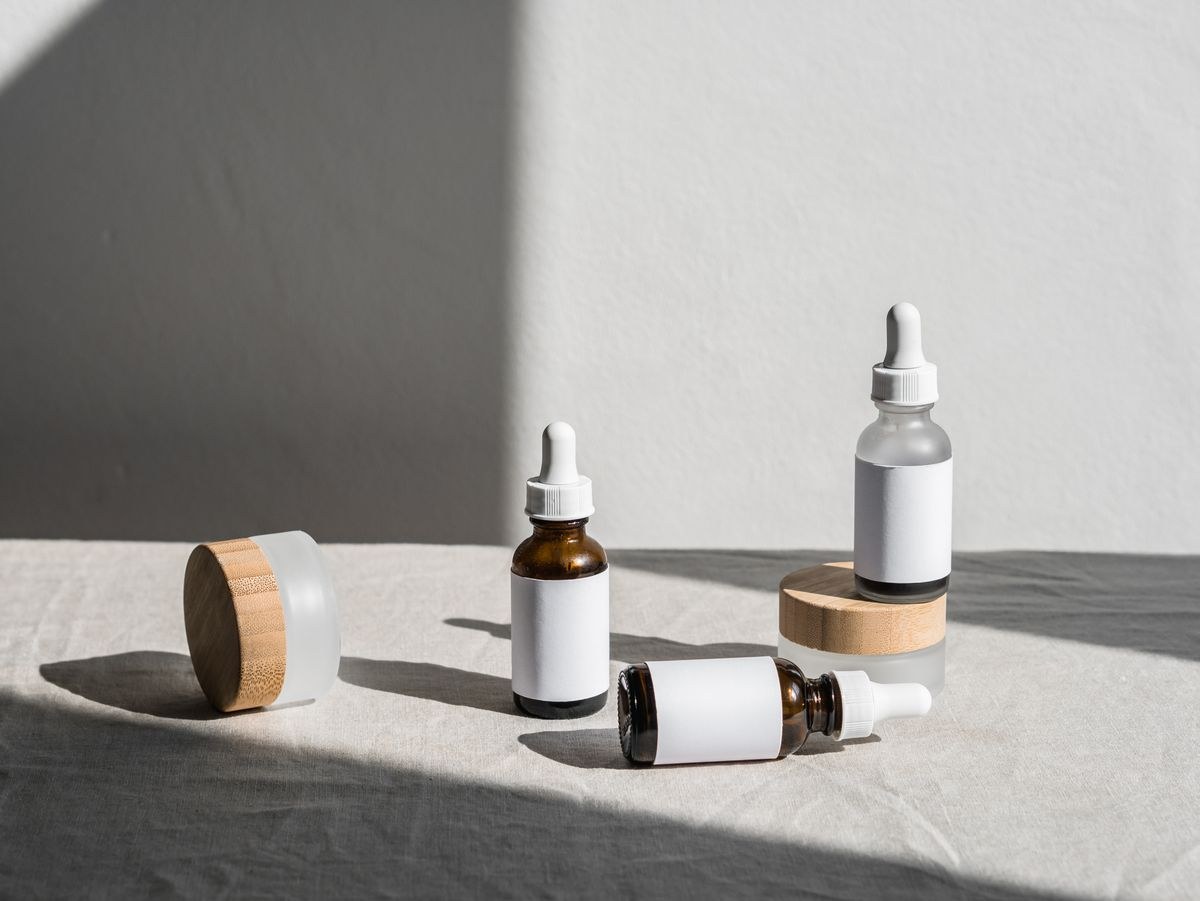 Unlabeled amber dropper bottles and bamboo-lid jars on linen in sunlight