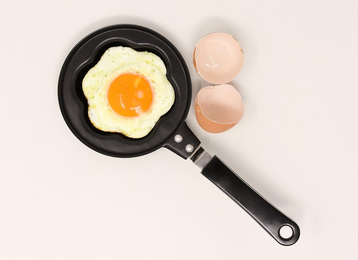 Fried egg in a small black frying pan beside cracked eggshells