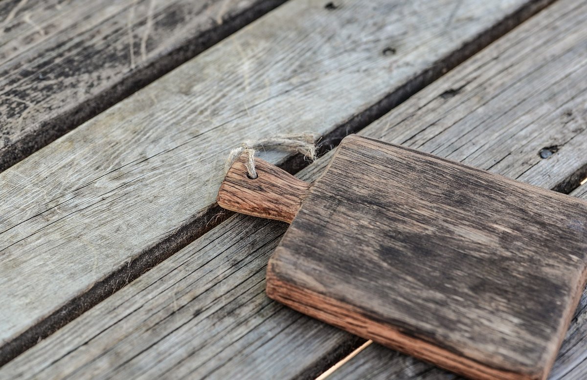 Weathered wooden chopping board with a rope handle on rustic planks